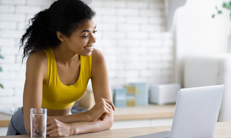 A woman in a yellow tank top sitting at a table with a laptop.