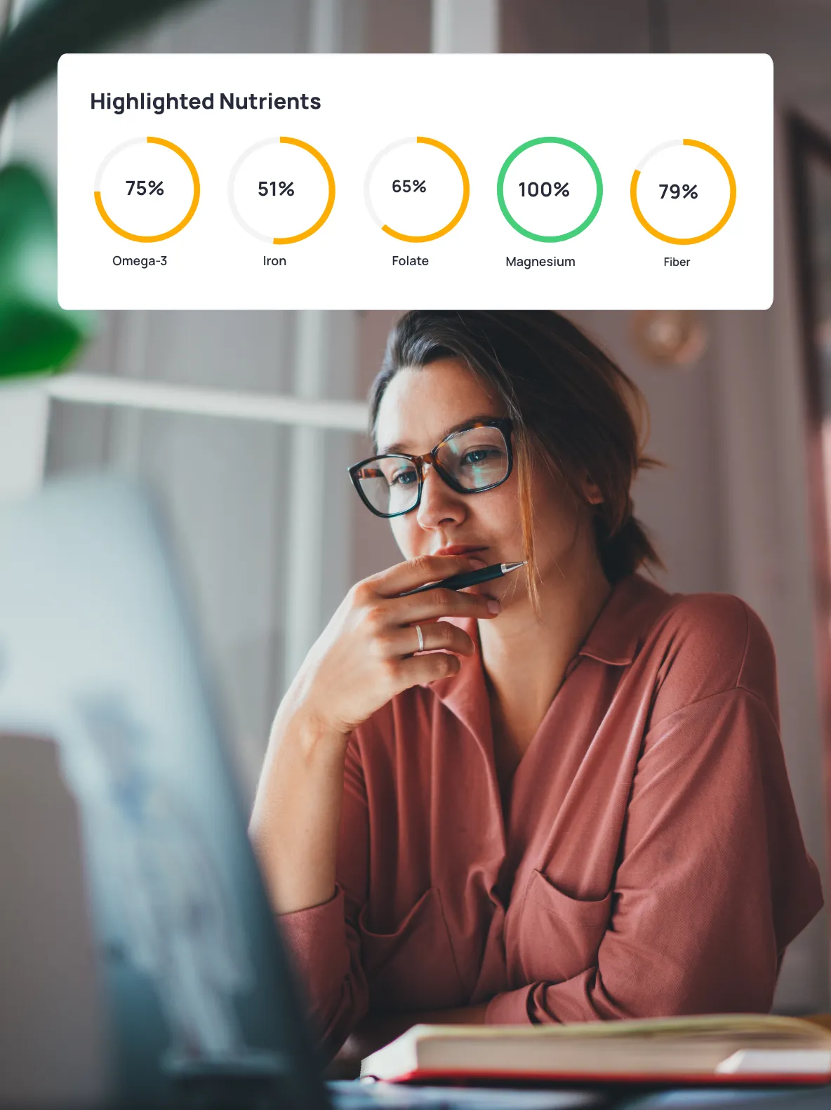 A woman wearing glasses and a pink shirt is looking at a laptop with nutrient targets from Cronometer on top.