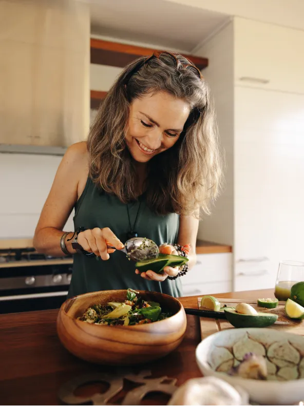 A woman is smiling while cutting vegetables in a kitchen.
