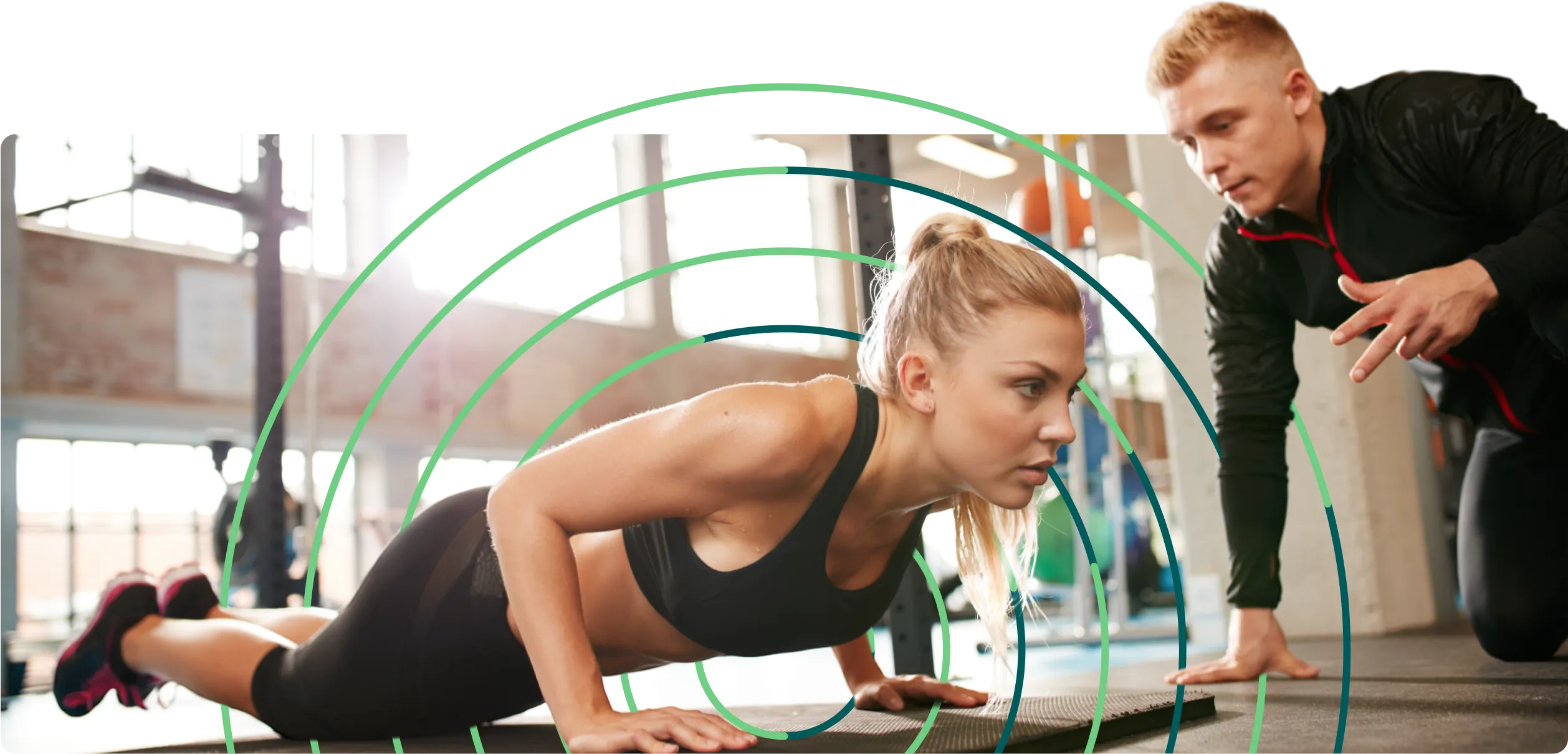 A woman doing a pushup in a gym with her fitness trainer.