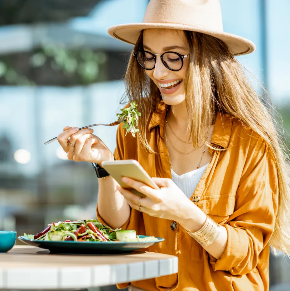 A woman wearing a hat and glasses is holding a cell phone.