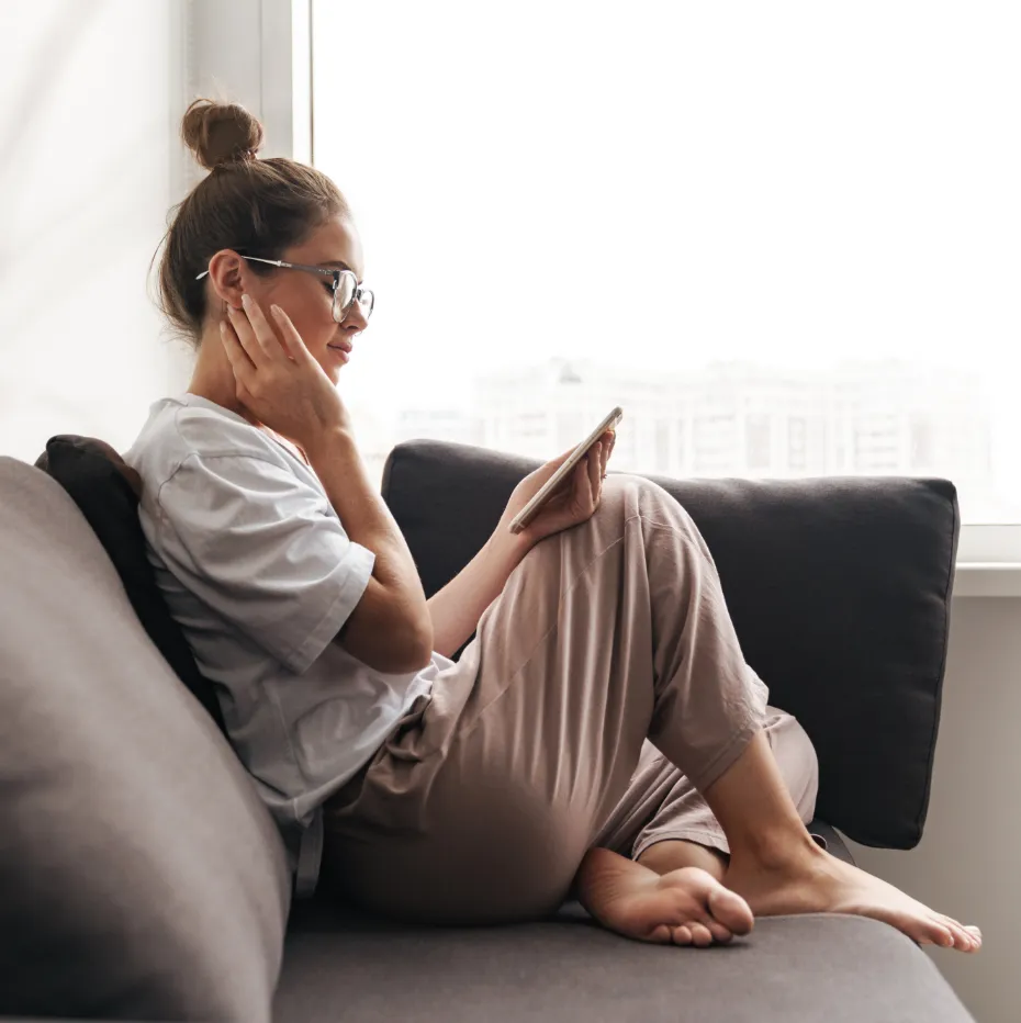 A woman wearing glasses and a ponytail sitting on a couch.