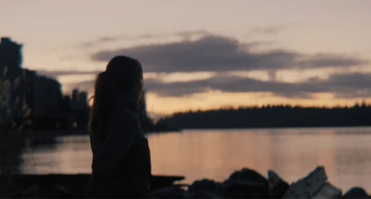 A woman standing on a rocky shore looking out at the water.