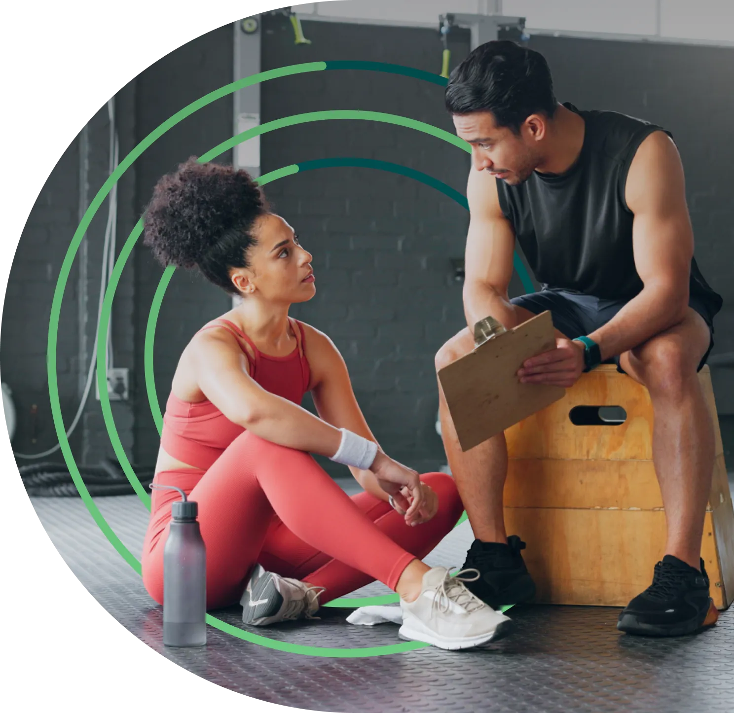 A fitness trainer and client sitting on the floor talking.