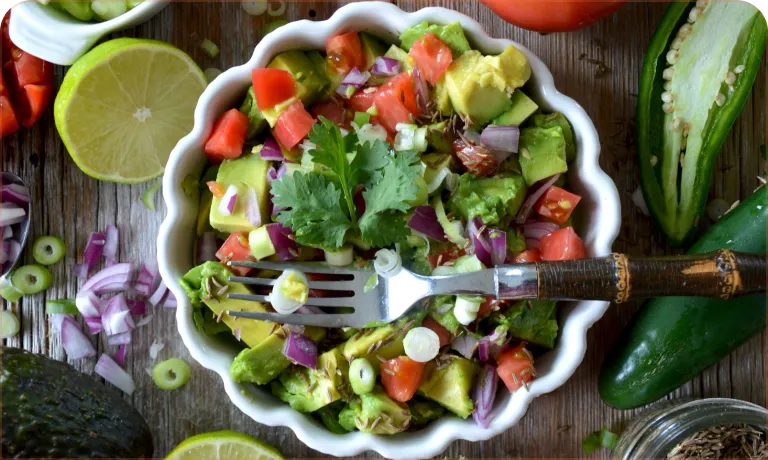 A white bowl filled with a salad of tomatoes, onions, and limes.