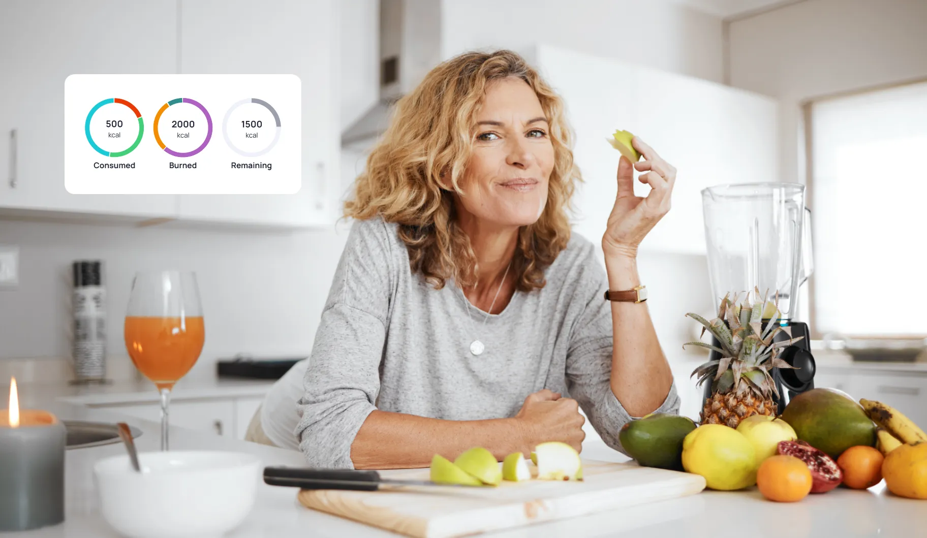 A woman is sitting in front of a table with a blender and a bowl of fruit with nutrient values from Cronometer on it.