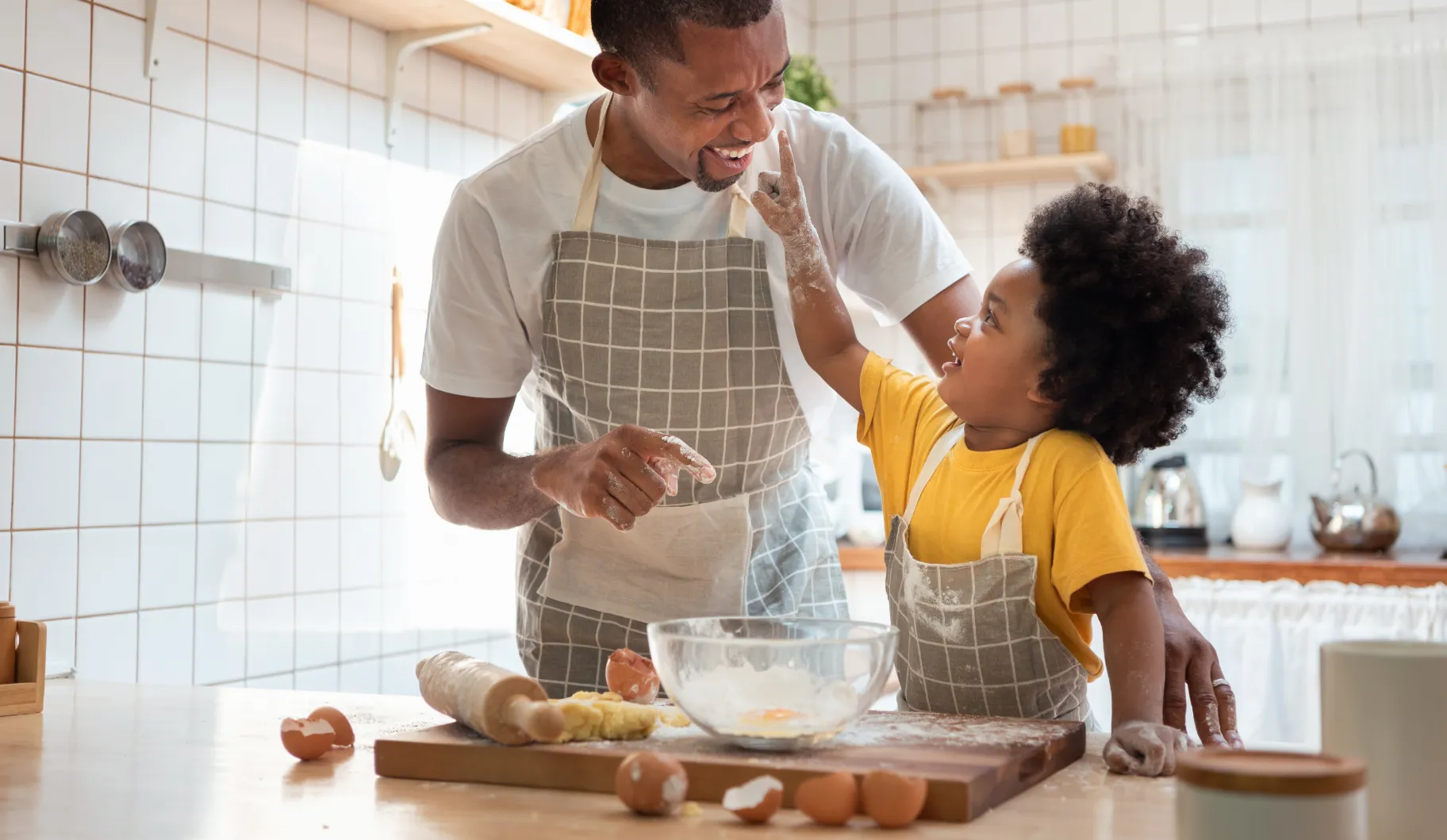A man and a boy are in the kitchen, the man is holding a bowl of flour.