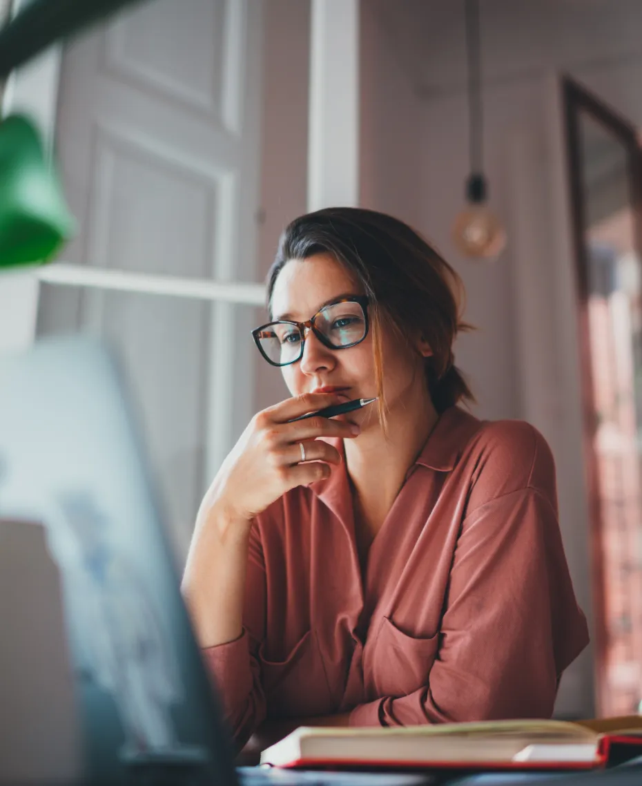 A woman wearing glasses and a pink shirt is sitting in front of a laptop.