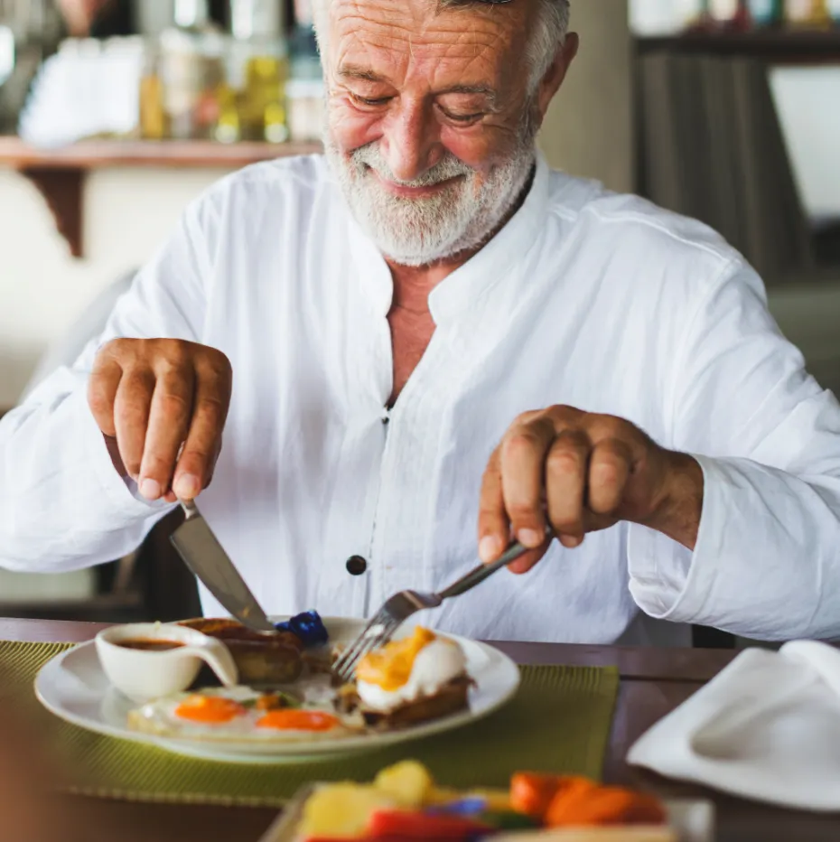 A man with a white beard and mustache is cutting food on a plate.