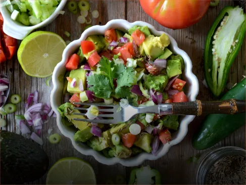 A white bowl filled with a salad of tomatoes, onions, and avocado.