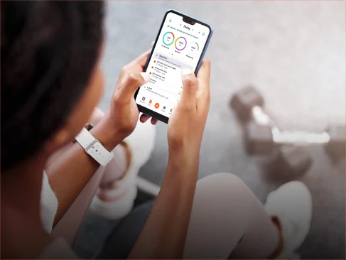 A woman holding a cell phone with a fitness app on the screen.