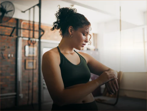 A woman wearing a green tank top and a green bracelet checks the time on her wristwatch.