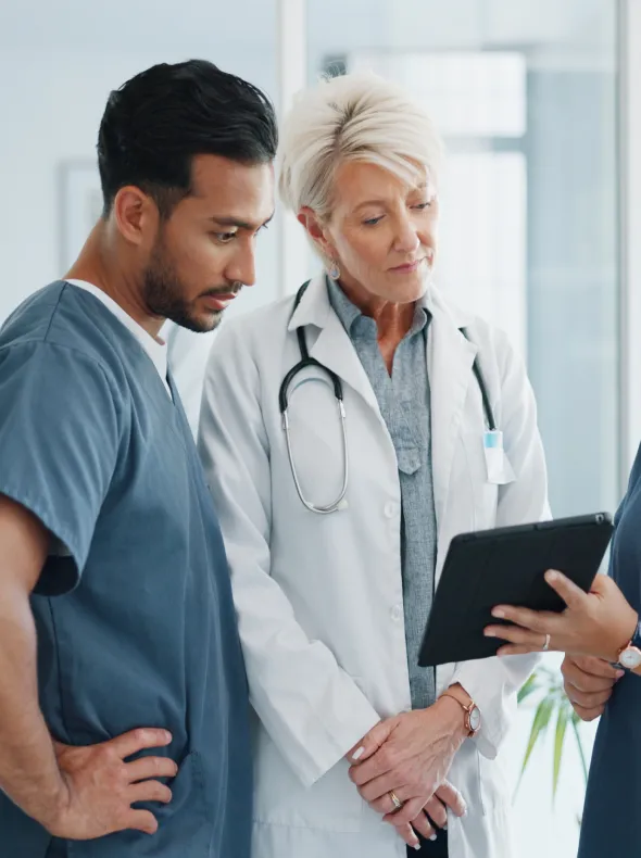 A man in a white coat is looking at a tablet with two other people.