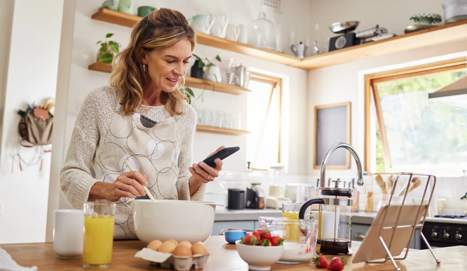 A woman is standing in a kitchen with a cell phone in her hand.